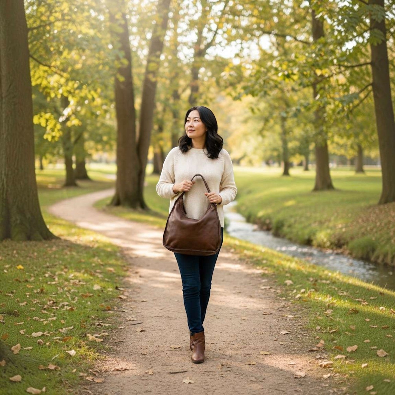 Donna che cammina in un parco con borsa Pito’s|Bag in pelle di vitello marrone con dettagli in ottone anticato