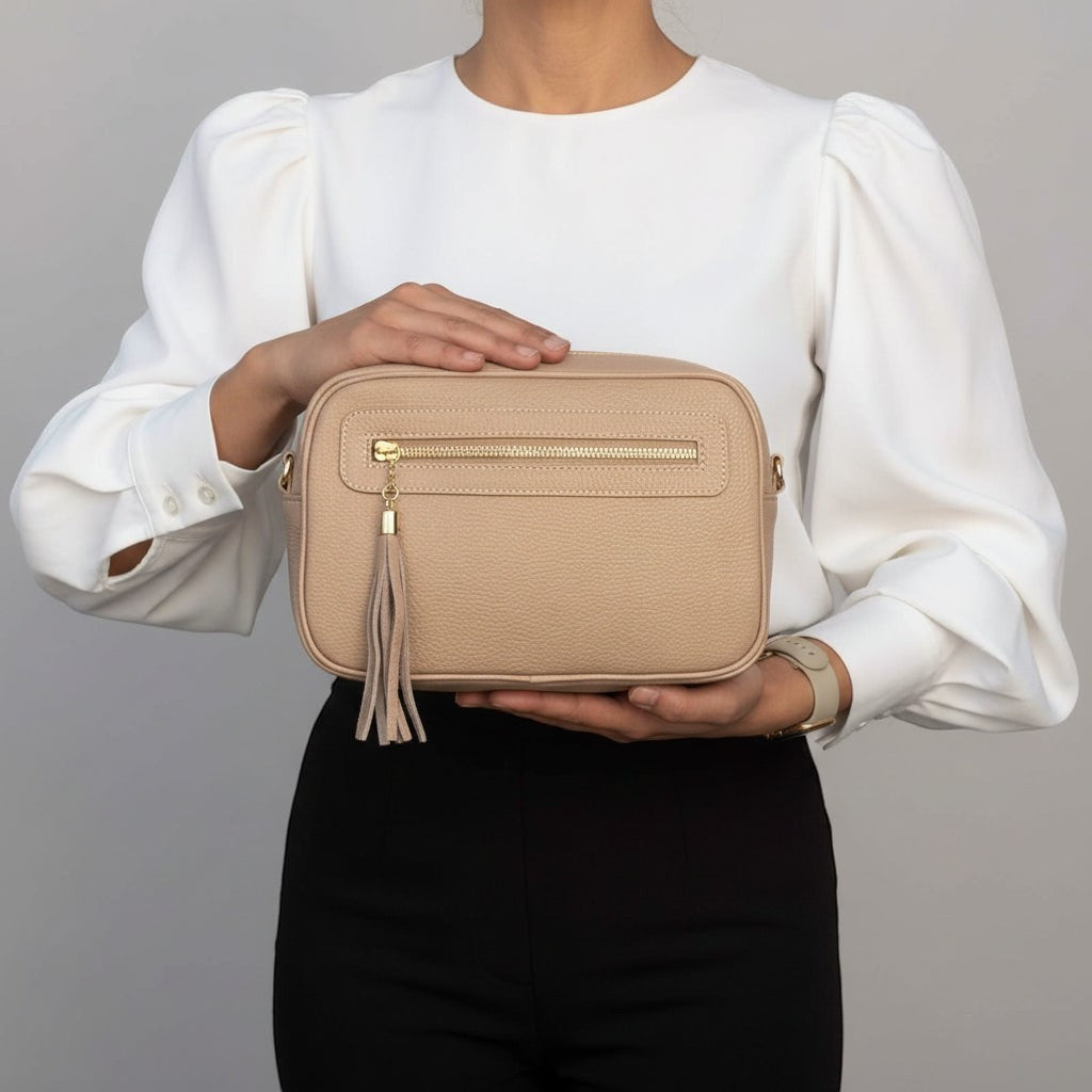 Tracollina Pito’s|Bag in vera pelle beige con zip, nappina decorativa e tracolla rimovibile, tenuta in mano.