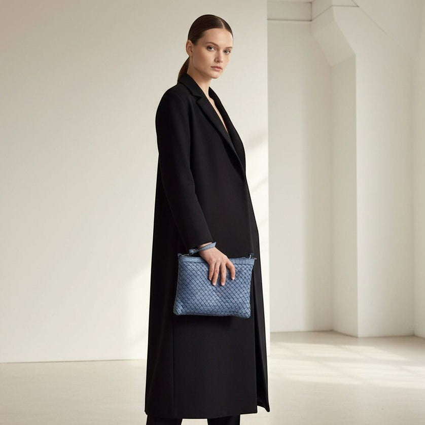 Modella con cappotto nero tiene la pochette Pito’s|Bag Giovy in pelle azzurra con lavorazione a intreccio regolare.
